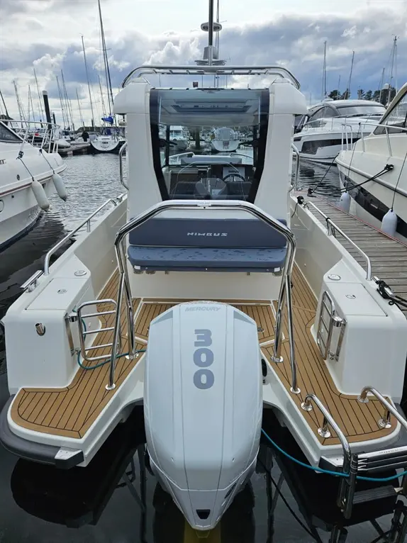 A white Nimbus boat with a Mercury 300 engine docked at a marina, surrounded by other boats and cloudy skies.